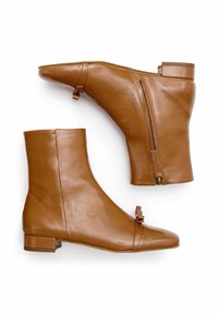 Botas de tobillo de cuero marrón con punta afilada, cremallera lateral y detalle decorativo de hebilla. Textura lisa con un tacón bajo tipo bloque.