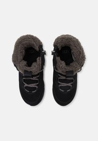 Crne čizme do članaka s teksturiranom ante površinom, podstavom od umjetnog krzna, dekorativnim vezicama i bočnim patentnim zatvaračima.