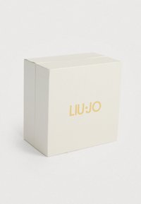 Λευκό κουτί με υφή που φέρει το χρυσό λογότυπο "LIU•JO" στο μπροστινό μέρος, με τετράγωνο σχήμα και καθαρό, μοντέρνο σχέδιο.