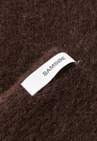Brunt, lodden stoff med en hvit etikett som sier "SAM SøE" sydd i kanten. Teksturen er myk med tette fibre.