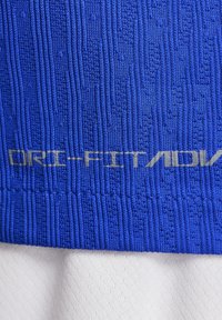 Tela DRI-FIT azul con un patrón de relieve texturizado; superpuesta a un material blanco y suave en la parte inferior. Énfasis en el diseño que absorbe la humedad.