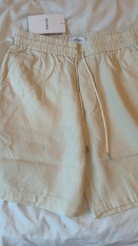 Hellbeige Shorts aus einem strukturierten Stoff, mit einem elastischen Bund und Kordelzug. An einem Etikett befestigt, ohne Muster oder Akzente.