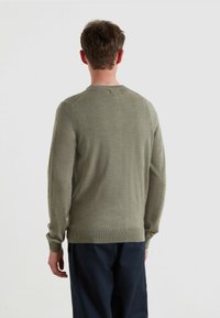 Zielono-oliwkowy sweter dzianinowy z długimi rękawami i okrągłym dekoltem. Miękka faktura oraz ściągacze u rękawów i na dole. Widok z tyłu.