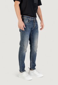 Jeans de denim azul desteñido con corte ajustado, que cuentan con cremallera, cinco bolsillos y un ligero desgastado en los muslos. Combinados con zapatillas blancas.