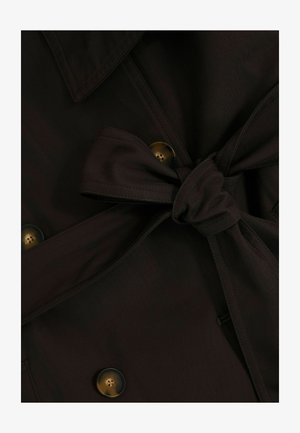 Tumši brūns audums, sasaistīts mezglā, ar redzamām pogām un pārklājošām šuvēm, kas norāda uz detalizētu apģērba aizdari.