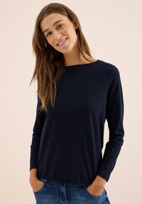 Navy long-sleeve shirt made from soft fabric, featuring a crew neckline and relaxed fit, paired with light blue jeans.