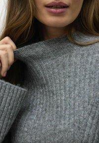 Pull en maille grise à col montant. Texture douce, avec des motifs en tricot verticaux et une coupe oversize autour de l'encolure.