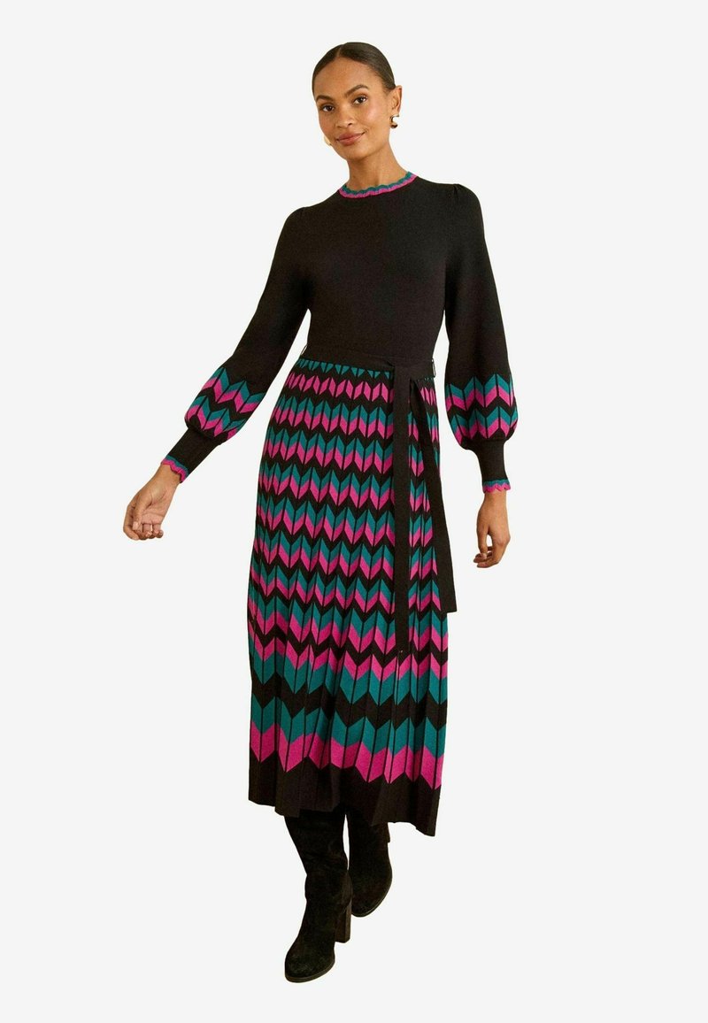 Rochie cu maneci lungi, de culoare neagră, având un model colorat în zigzag în nuanțe de roz, teal și negru. Rochia are talie ajustată și fustă evazată.