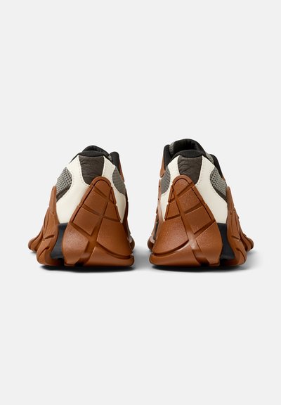 Braune und weiße Sportschuhe mit einem strukturierten Mesh- und Lederoberteil, das ein auffälliges, geschichtetes Gummisohlendesign aufweist.