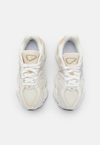 White and cream sneakers with mesh and leather upper, textured detailing, round toe, thick sole, and contrast logo on tongue.