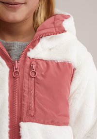 Műszőrme dzseki rózsaszín nylon panelekkel, dupla cipzárral, kapucnival és puha fehér textúrával. A dzseki szoros illeszkedésű.
