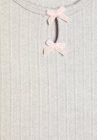 Haut en tricot gris clair présentant une texture en côtes verticales, une ouverture en forme de clé, et deux petits nœuds en satin rose au niveau du col.