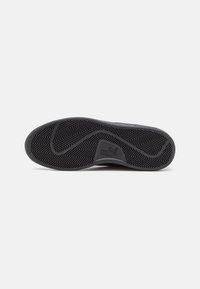 Black rubber sneaker sole featuring a herringbone tread pattern and a raised logo. Smooth texture with curved edges and sturdy design.