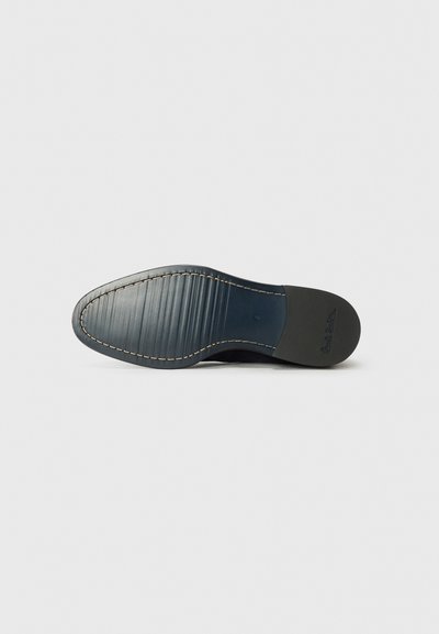 Suela de zapato de cuero negro con un acabado texturizado, que presenta una plantilla azul y costuras blancas a lo largo de los bordes de la suela exterior. Forma plana y redondeada.
