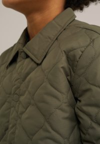 Olive green quilted jacket featuring a collared neckline, button closures, and textured patterns on the fabric for insulation.