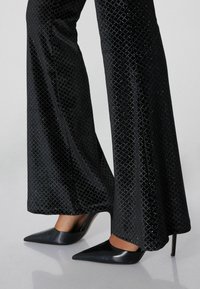 Zwarte uitlopende broek met een getextureerd diagonaal patroon, gecombineerd met zwarte puntschoentjes met een glanzende afwerking en naaldhakken.