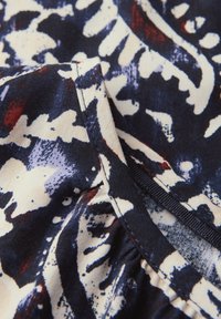 Tessuto multicolore che somiglia a un motivo floreale con tonalità di blu scuro, bianco e rosso. Presenta una consistenza morbida e dettagli arricciati lungo il bordo.