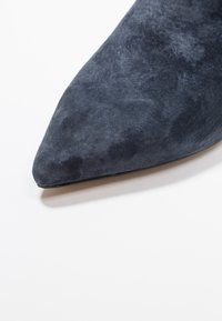 Tacón stiletto de ante azul marino con punta afilada y textura suave, que muestra un diseño elegante y una estética minimalista.