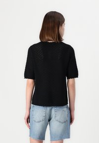 Top nero in maglia con maniche corte, motivo testurizzato, orli a zigzag; abbinato a pantaloni corti in denim blu chiaro con bordi sfilacciati.