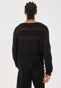 Schwarzer gestrickter Pullover mit horizontalen Streifen, gerippten Bündchen und Saum. Lockere Passform mit einer strukturierten, leicht durchscheinenden Optik.