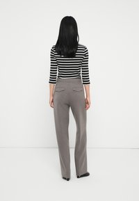 Szare dopasowane spodnie z wysokim stanem, z marszczeniami z przodu i dwiema tylnymi kieszeniami, zestawione z czarno-białą bluzką z długim rękawem w pasy.