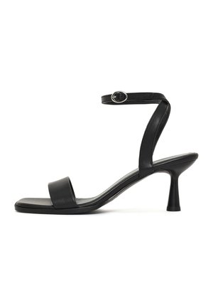 Sandale à talon haut noire avec bout carré, bride à la cheville avec boucle argentée et talon fin sur fond blanc.