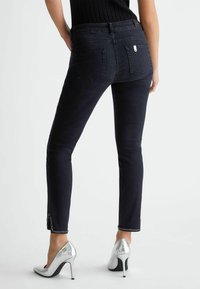 Úzké černé džíny z denimového materiálu s polovičním pasem, jemnými švy a rozparkem na spodním lemu. Kombinované s stříbrnými vysokými podpatky.