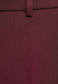 Detailní záběr na burgundskou látku s poutkem na pásek a švem pasu, ukazující podrobně texturu tkaniny a diagonální vzor tkaní.