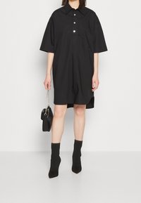 Czarna sukienka zapinana na guziki z krótkimi rękawami, kieszonką na piersi i luźnym krojem. Połączona z teksturowanymi czarnymi skarpetkami do kostek oraz małą czarną torebką.