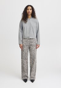 Sweatshirt gris cropped avec boutons associé à un pantalon large à imprimé léopard. Texture lisse et coupe décontractée dans des tons neutres.
