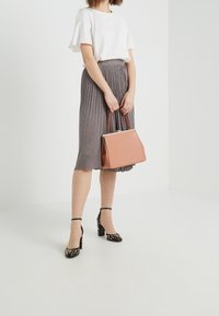 Gonna grigia a pieghe, top bianco a maniche corte, tacchi neri con borchie dorate e una borsa strutturata rosa con dettagli cuciti.