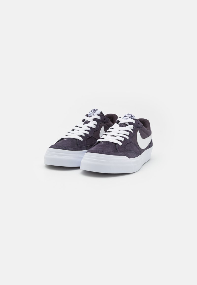 Las zapatillas de ante morado oscuro presentan suelas de goma blanca, cordones blancos y un logo en forma de swoosh blanco en el lateral. La parte superior texturizada ofrece agarre.