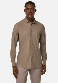 Camisa de manga larga, con botones, en un tono marrón apagado, que presenta una textura suave, cuello estándar y botones oscuros delante.