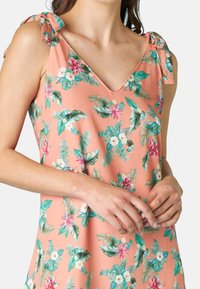 Top senza maniche a fiori di corallo con scollatura a V, caratterizzato da foglie verdi e fiori rosa, spalline annodate e una texture di tessuto liscia.