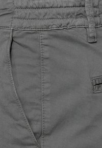 Gros plan sur un pantalon en tissu gris mettant en évidence une poche latérale, une boucle de ceinture et des coutures détaillées.
