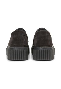 Zwarte suède schoenen met een stevige geribbelde zool, voorzien van een klein geperst logo en gestikte details aan de achterkant. Platte hak.