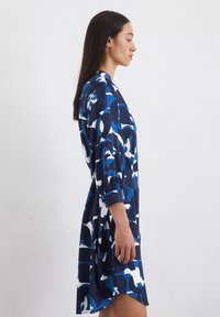 Abito blu navy realizzato in morbido tessuto, caratterizzato da motivi astratti blu e bianchi, maniche lunghe con polsini arricciati e orlo leggermente curvo.