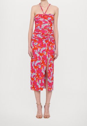 Femme portant une robe midi à bretelles à imprimé abstrait aux couleurs rose, orange et bleu, avec une fente à l'avant et des sandales à talons hauts beiges.
