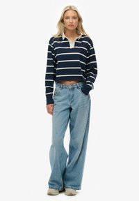 Marineblauw-wit gestreept cropped rugbyshirt met lange mouwen, gecombineerd met lichtblauwe jeans met wijde pijpen en beige sneakers.