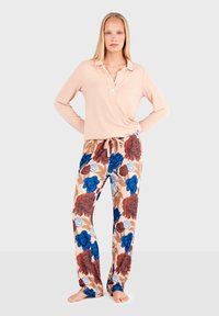 Haut rose pâle à manches longues avec col et un bouton, associé à un pantalon beige orné de grands motifs floraux bleus et rouges.