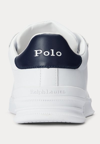 Hvid sneaker med en marineblå hælflig mærket "Polo" og "Ralph Lauren" præget på sålens område bagpå.