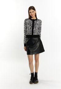 Cardigan con stampa leopardata in viola, nero e bianco, con borde nero. Abbinato a una minigonna in pelle nera elegante e stivali neri con lacci.