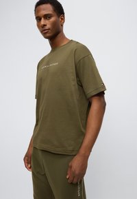 Λαδί κοντομάνικη βαμβακερή μπλούζα με στρογγυλή λαιμόκοψη, με το λογότυπο "TOMMY HILFIGER" κεντημένο με άσπρα γράμματα στο στήθος και λογότυπο της μάρκας στο μανίκι.