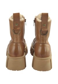 Bottes chelsea en cuir brun avec doublure en fausse fourrure, fermeture éclair et semelle en caoutchouc épaisse avec profondes rainures. Détail de boucle à l'arrière et d'emblème.