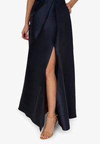 Granatowa satynowa spódnica maxi z wysokim rozcięciem, charakteryzująca się gładką teksturą i zwiewnym krojem. Noszona z tanim obuwiem na obcasie z paskiem na kostce.