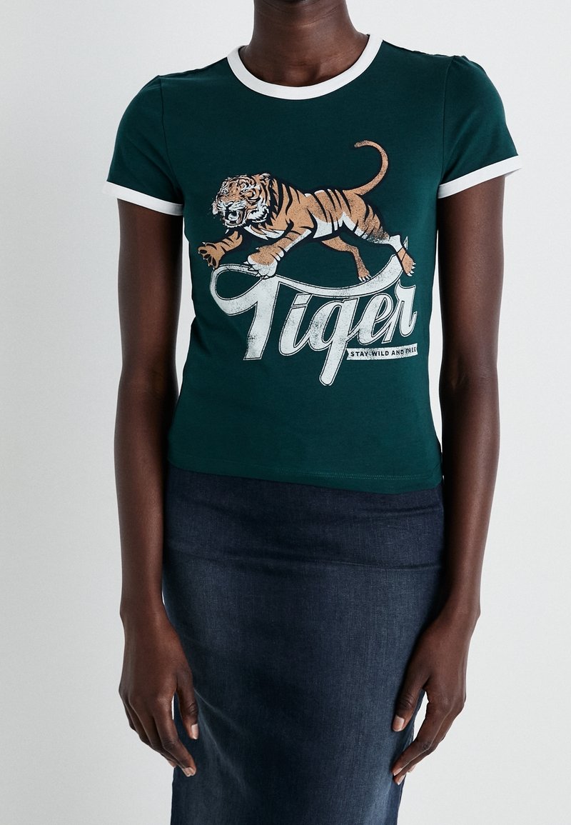 Camiseta de algodón verde con un cuello y mangas acanaladas blancas. Presenta un gráfico de un tigre y el texto "Tiger" en una fuente negrita. Textura suave.