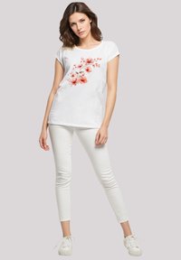 White short-sleeve t-shirt with floral print in shades of orange, paired with white slim-fit jeans and white sneakers. Smooth fabric, casual design.