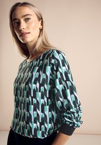 Mönstrad långärmad topp i nyanser av grönt, svart och vitt, med rund halsringning och strukturerad tygkvalitet samt åtsittande ärmslut.