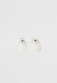 Vita sneakers med slät läderövre, texturerad vit gummisula och en grå hälflik med en svart logotyp. Enkel och minimal design.