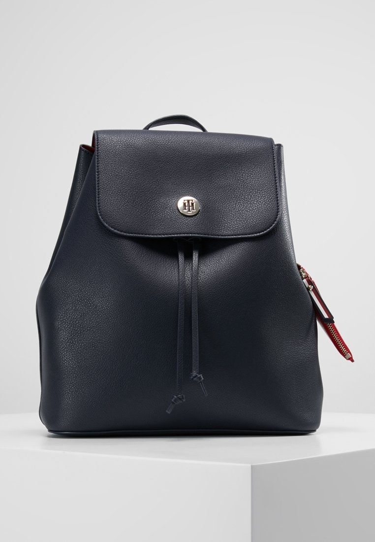 Zaino in pelle blu navy con chiusura magnetica, dettaglio con cordoncino, tasca laterale con zip rossa e accentuazione del logo. Texture liscia.